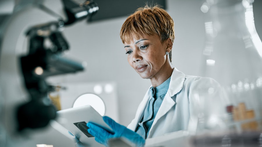 A woman scientist holding and looking at a tablet while wearing protective gloves to ensure risk management in medical device design.