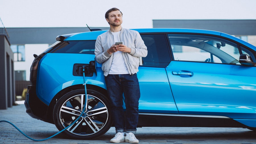 Man standing outside of his electric vehicle as it charges at a charging station.