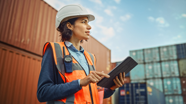 Person holding a tablet in a shipping container yard.