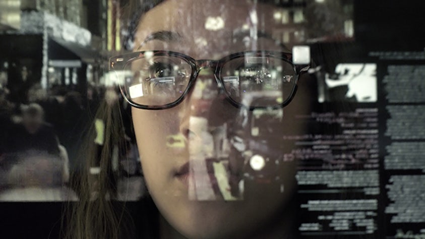 A woman in glasses is looking at a screen with text on it.