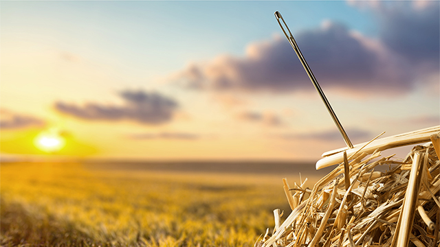 Image showing a needle sticking out of a hay stack with a field and sunset in the background. 