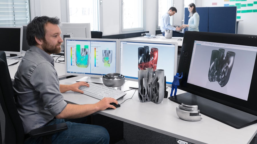 A design engineer uses CAD software for generative design to ideate different part designs at his computer work station with four monitors.