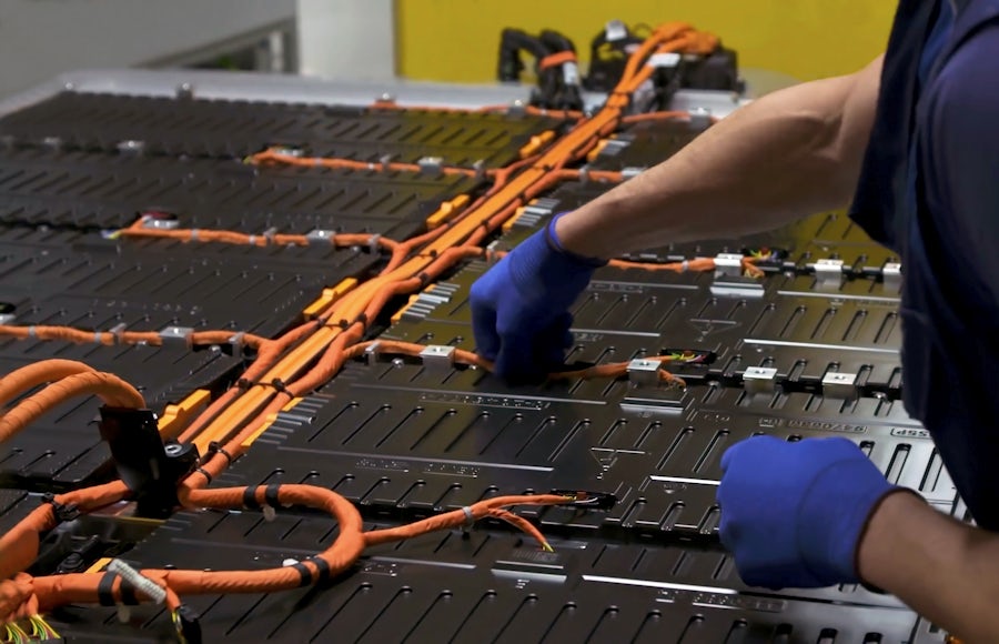 A pair of hands working on complex battery production lines with the body out of shot. 