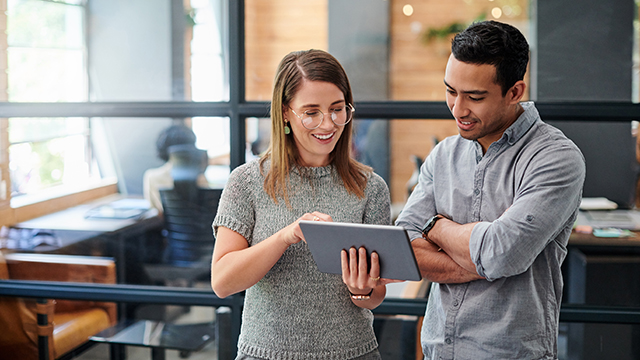 Two coworkers working together on a digital tablet in an office.