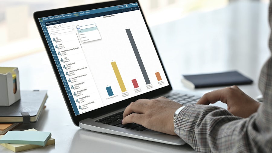 Worker typing on a laptop computer with a screen displaying a graph from Teamcenter Quality software. 