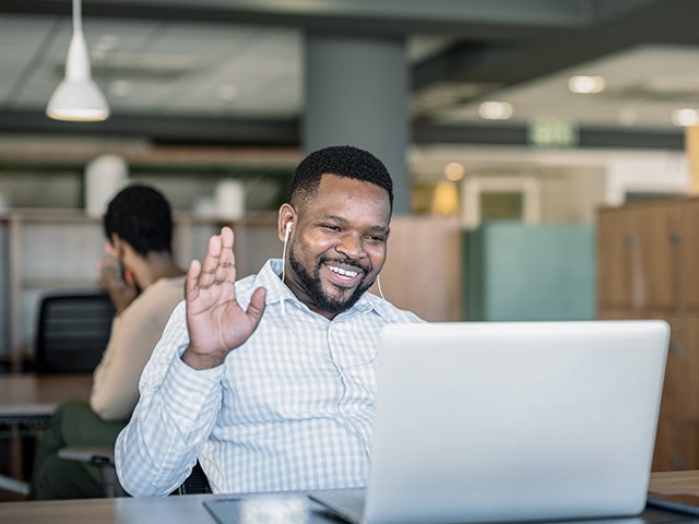 Man working on laptop and waving to team members on screen