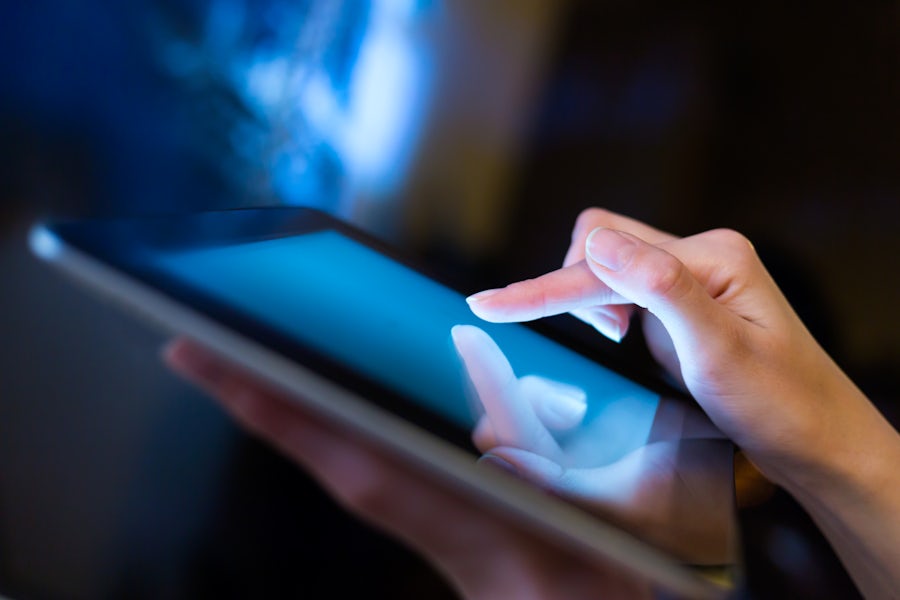 Close-up of hands interacting with a tablet's illuminated blue screen.
