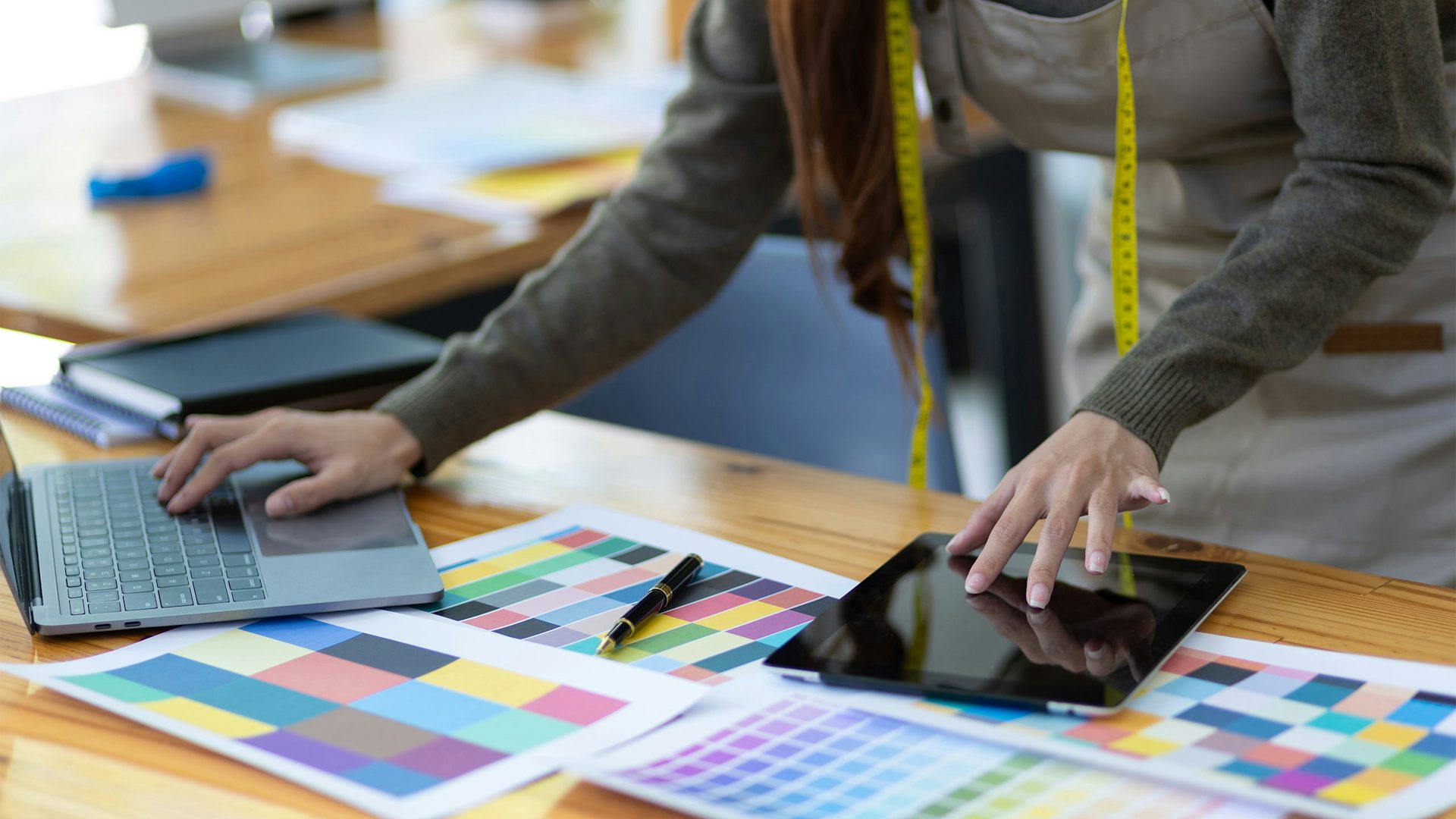 Fashion designer using digital tools to manage color palettes on a laptop and tablet during the product development process.
