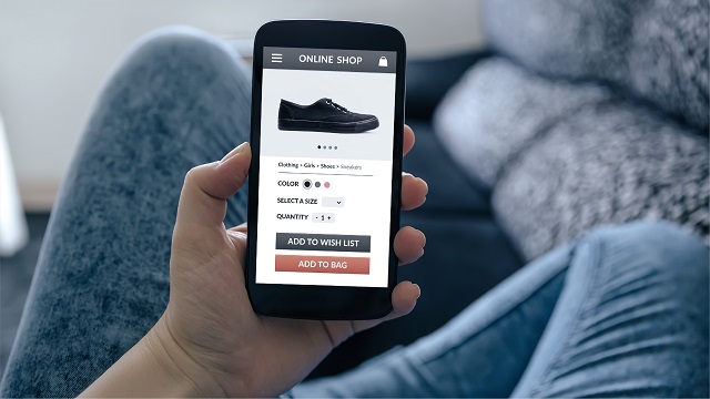 A hand holding a cell phone, displaying a shoe store website