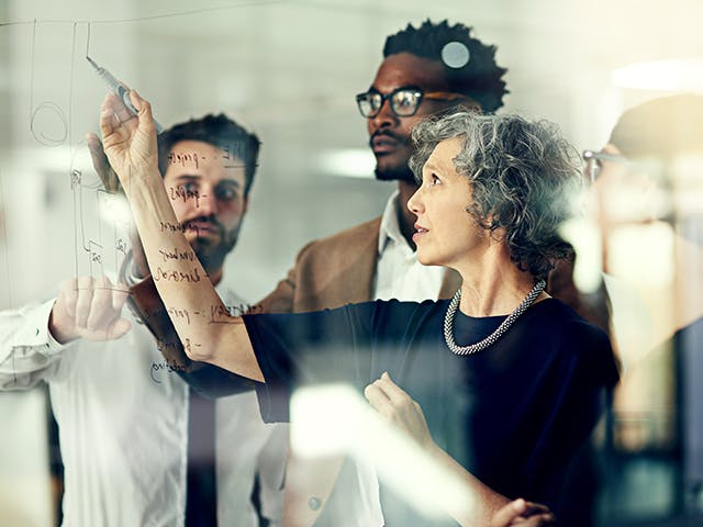 A group of people pointing at a whiteboard. 