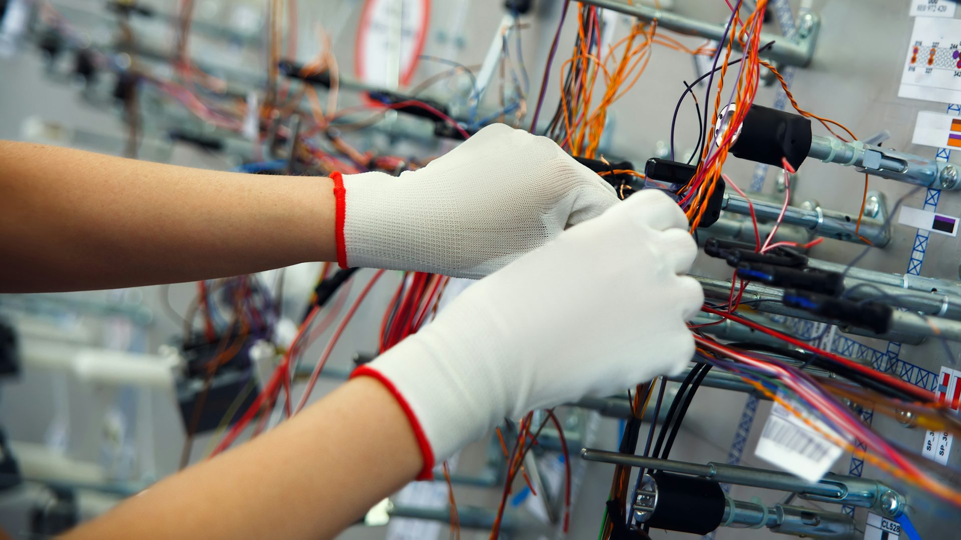 Una persona con guantes blancos ensambla un diseño de tablero de construcción de arneses.