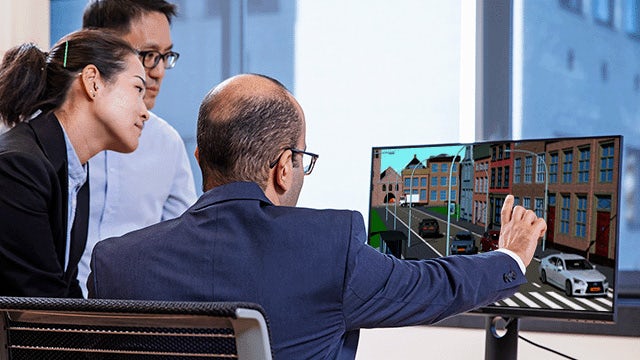 Trzy osoby patrzące na komputer i rozmawiające o wykorzystaniu zintegrowanych rozwiązań E/E do pokonywania stojących przed nimi wyzwań.