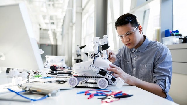 An  engineer works on programing a robot at a tech startup. The entrepreneur participates in Siemens startup program where he uses a wide range of startup solutions and tools tailored specifically for early stage startups. The startup has access to free developer licenses where they are able to build on top of Siemens products to get to market faster.  
