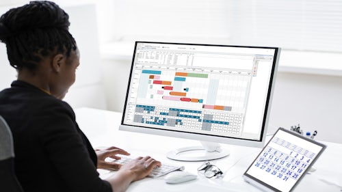 Advanced planning and scheduling software is displayed on a screen for an employee sitting at her desk. 