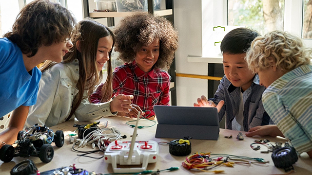 A group of teenagers gathered around a table with electronic components and a tablet computer