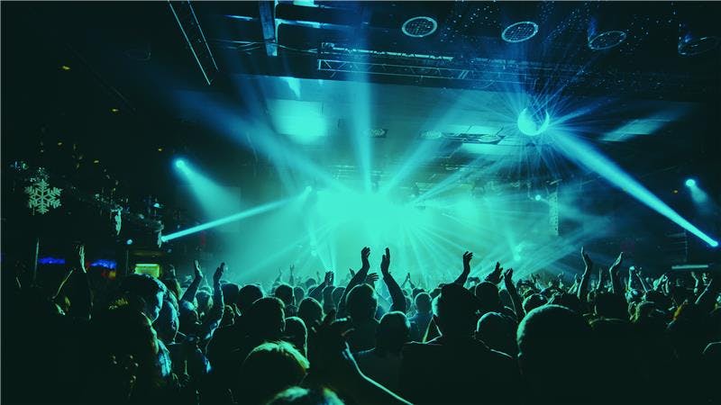 A crowd in action at a concert; blue lights are flashing onto a stage.