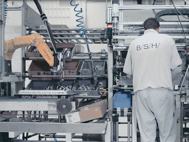 Dělník v továrně B/S/H stojící před sestavovací linkou v dílně a sbírá nástroje.
