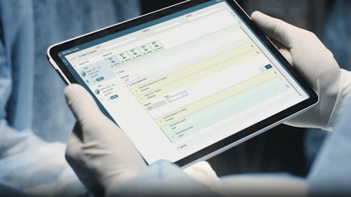 Manufacturing worker in a cleanroom environment views Opcenter Execution software on a tablet.