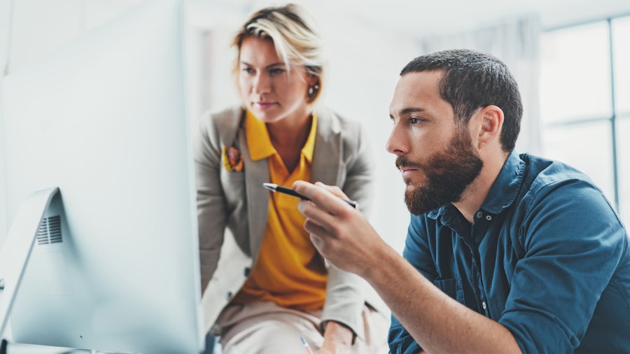 Zwei Kollegen arbeiten gemeinsam an einem Projekt an einem einizgen Computermonitor.