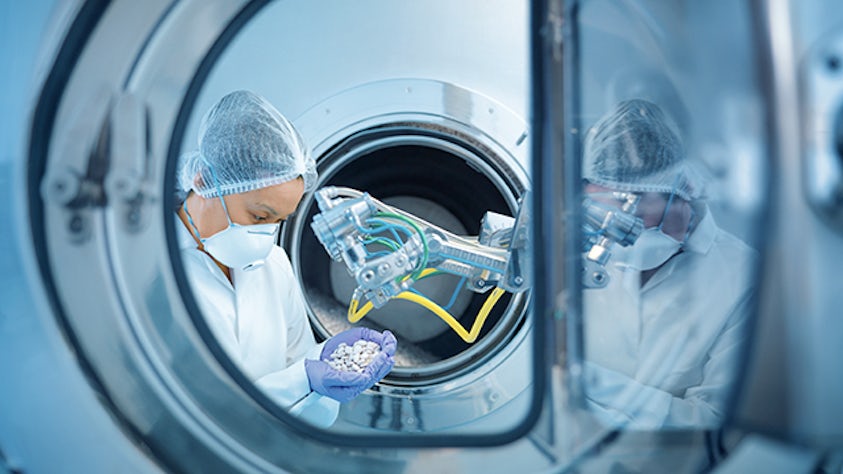 An enterprise resource planning factory worker holding beads outside of a machine.