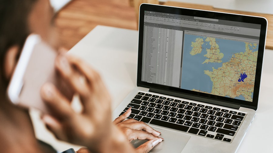 A woman engaged with her laptop, exploring a XCargo-software map on the screen, with a cozy workspace in the background.