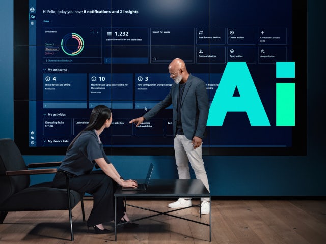 Two professionals review data on a large digital screen displaying system insights, with the Siemens shape, AI, highlighting the focus on artificial intelligence.