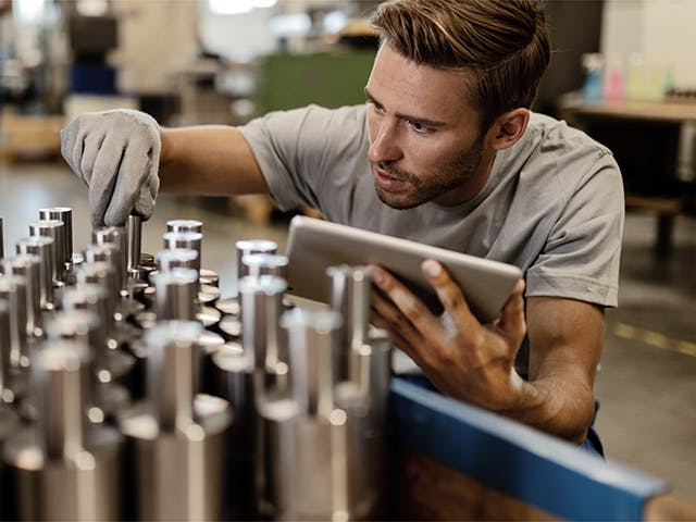 Hombre en un taller de mecanizado organizando cuidadosamente los componentes metálicos, mientras sostiene una tableta