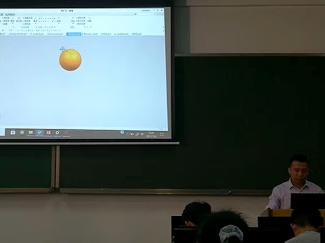 A professor in a classroom teaching NX CAD. He is projecting an orange sphere design in NX CAD onto a screen.
