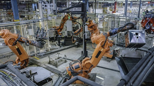 Industrial robotic arms move in unison on a manufacturing facility.