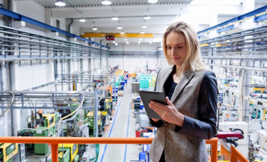 A woman is holding a tablet while she works in an electronics factory/lab.