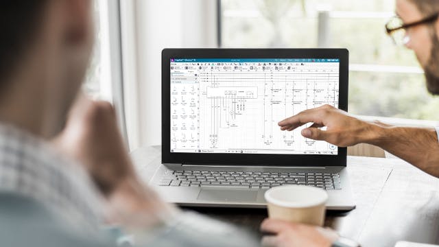 Two men sitting in front of a computer. One of them is showing the other a graph or chart on the computer screen.