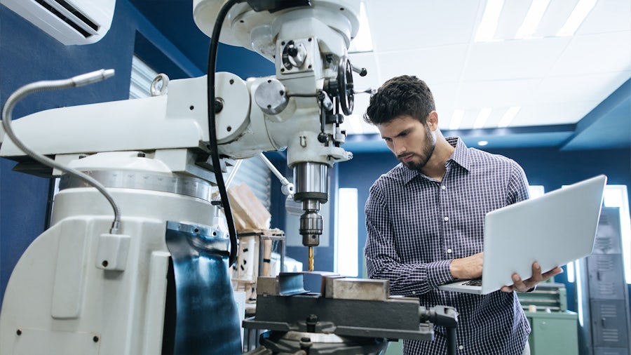 Man working on machine while holding a computer