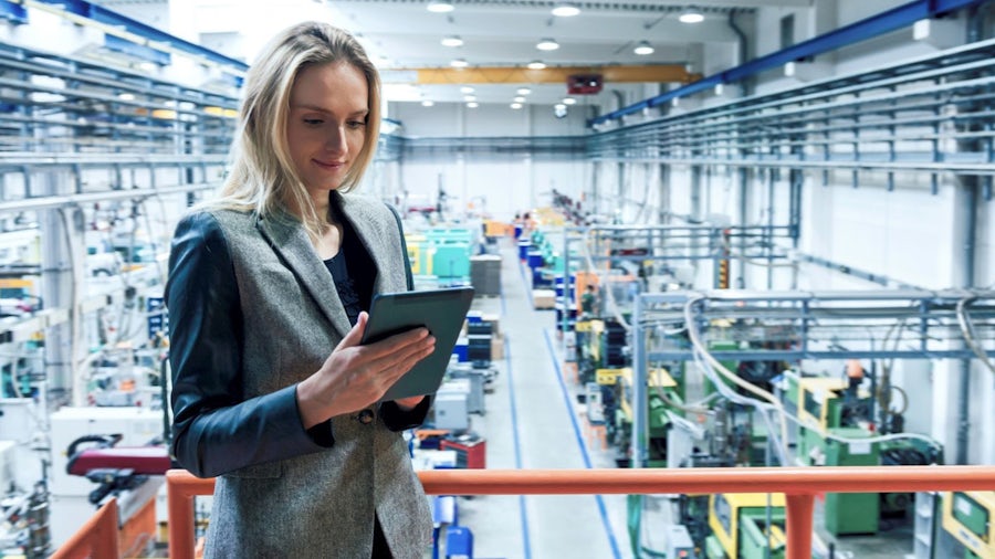 A manufacturing manager watches over the shop floor while monitoring OT data on a tablet.