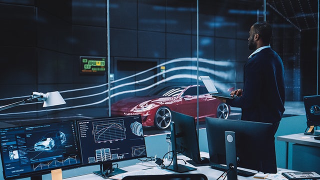 Engineer testing aerodynamics with a modern eco-friendly red electric sports car in a wind tunnel. The tester is working on a laptop and changes testing options.