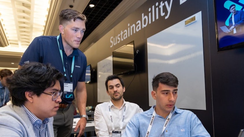 Four students sitting around a laptop at the Siemens Realize LIVE Americas digital transformation conference sustainability design hack.