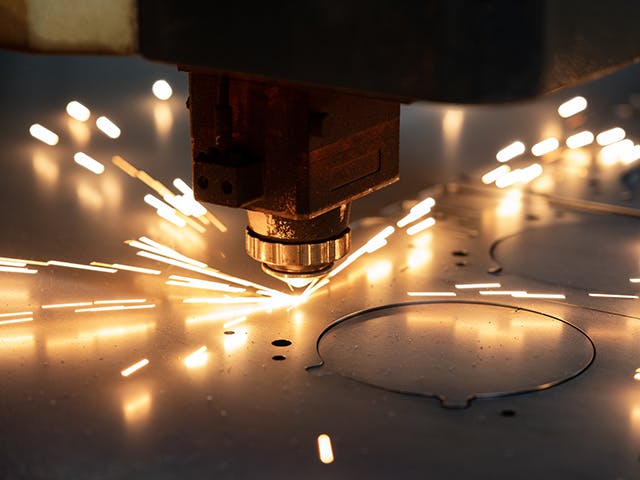 Close-up of a laser cutting machine slicing through sheet metal with sparks flying.