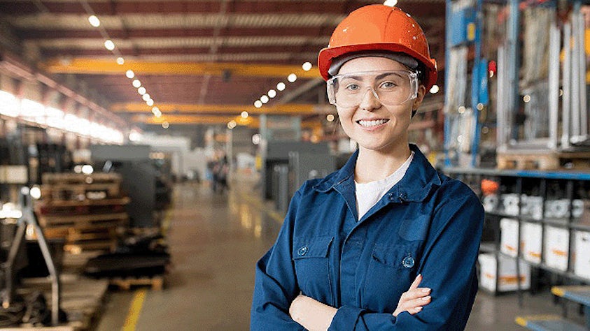 Una mujer con equipo EPI está de pie en una fábrica