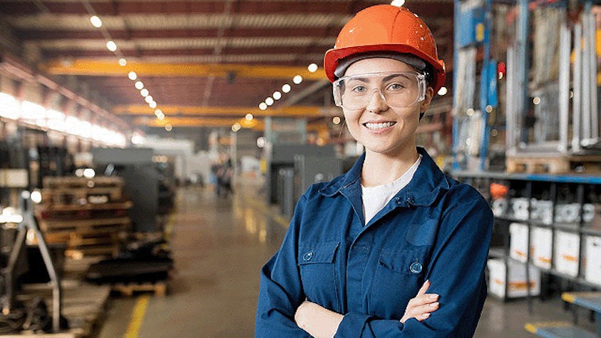 Une femme portant un équipement de protection individuelle (EPI) se tient dans une usine.