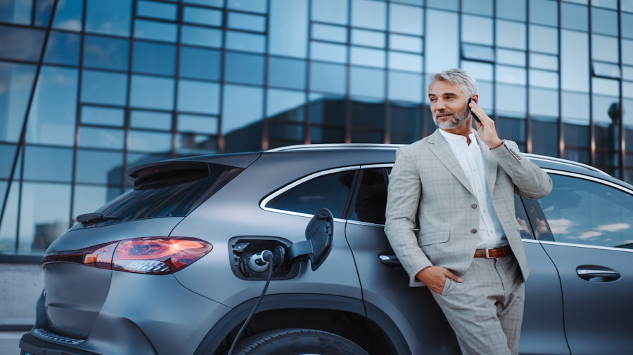 Businessman talking on the phone while charging his EV at a charging station.