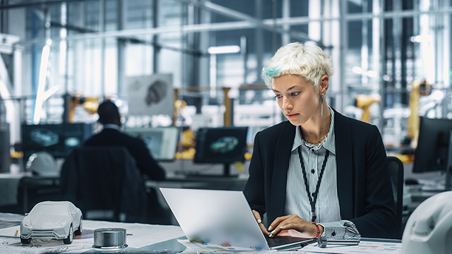 A woman sitting at a laptop computer, next to a clay model of a car