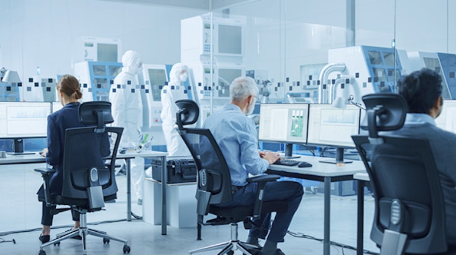 A women and two men work on their computers in a semiconductor lab while two engineers work in the lab.