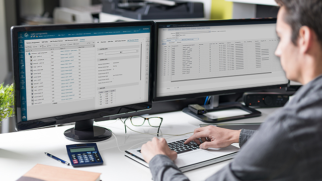 Muž sedící u stolu a dívající se na dvě obrazovky počítače v kancelářském prostředí.