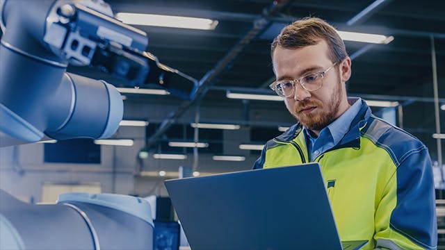 Engineer uses laptop for programming a robotic arm.