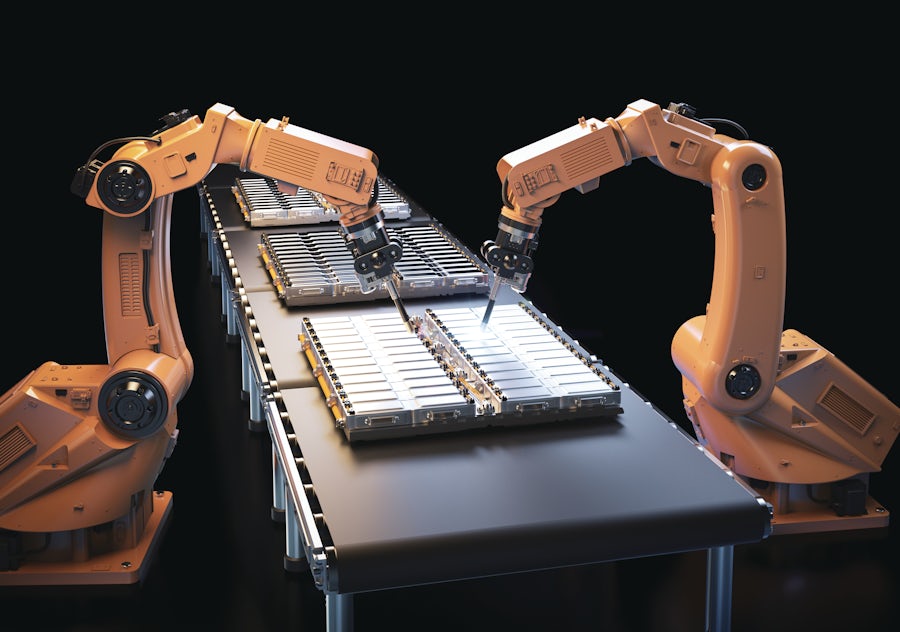 A pair of orange robotic arms assembling electric battery packs on a conveyor belt.