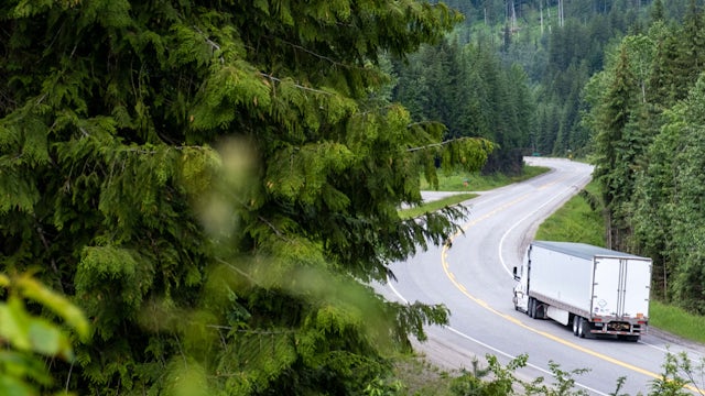 Semi truck and trailer on a road winding through a forrest.
