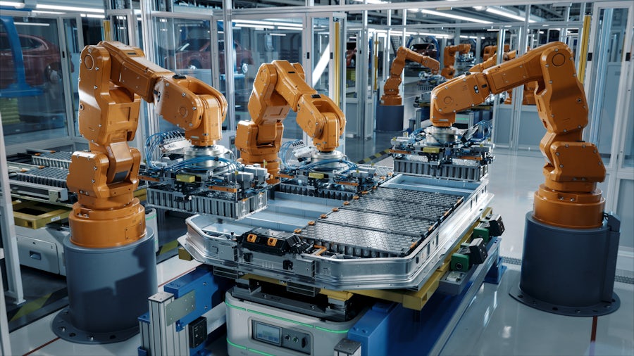 Advanced orange industrial robot arms in a modern electric car smart factory.
