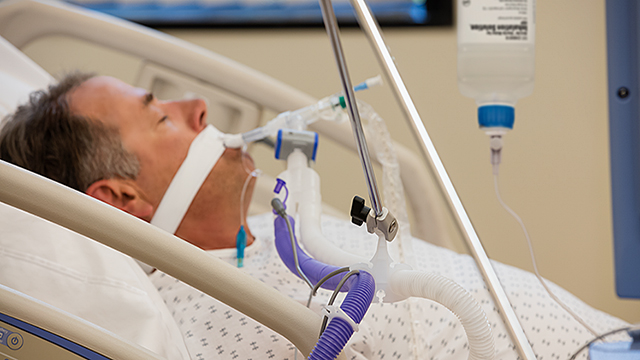 Un uomo giace in un letto d'ospedale con un tubo respiratorio in bocca