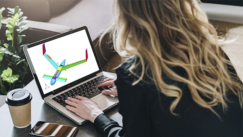 An engineer working on a laptop with a structural design analysis model of an aircraft displayed on the screen.