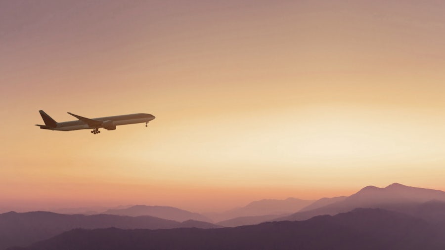 An aircraft soars above mountains in a sky colored in shades of orange