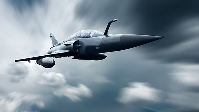 Military airplane flying at high speed through the clouds.